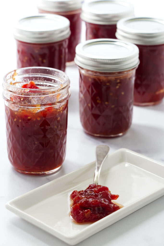 Several jars of spiced tomato preserves with more jam in front on a spoon.