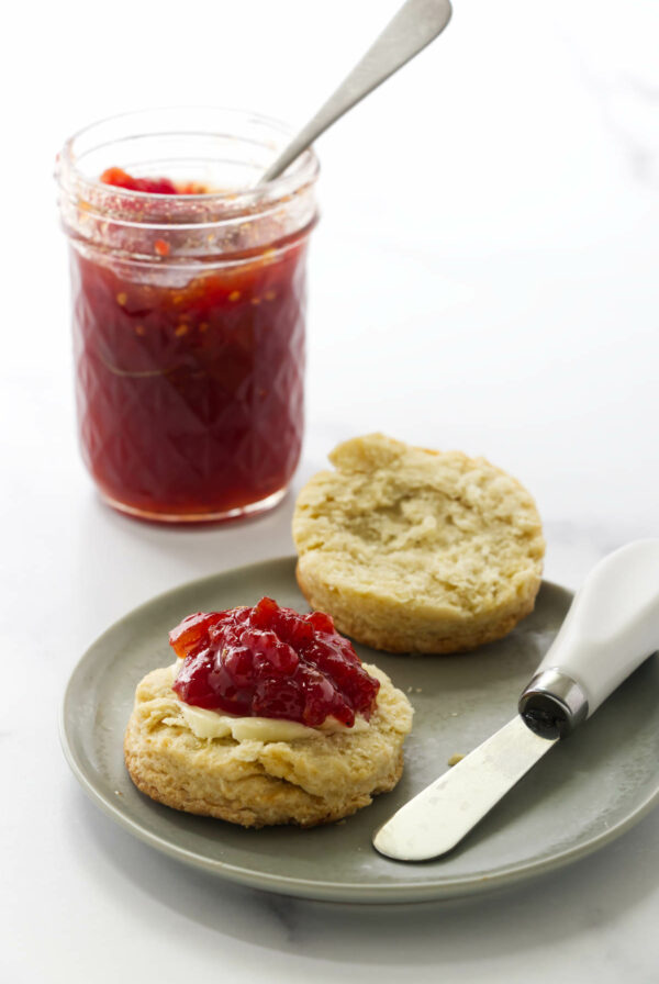 Tomato preserves on a biscuit in front of a jar of tomato jam.