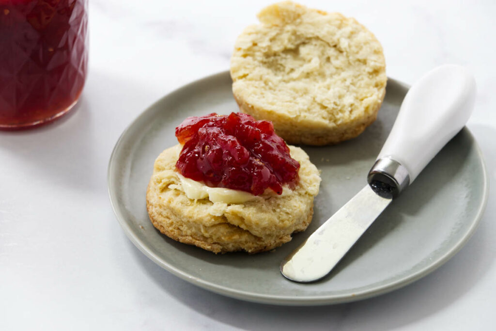 A biscuit topped with spiced tomato jam next to a butter knife.