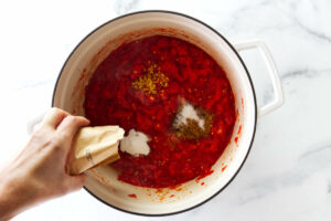 Adding spices and pectin to a pot of tomato jam.