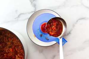 A ladle scooping tomato preserves into a canning jar.