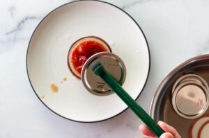 Placing a canning lid on a jar of tomato preserves.