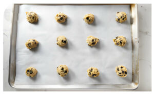 Twelve balls of chocolate chip cookie dough on a sheet pan.