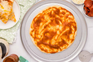 Adding pizza sauce to a dough stretched on a pizza pan.