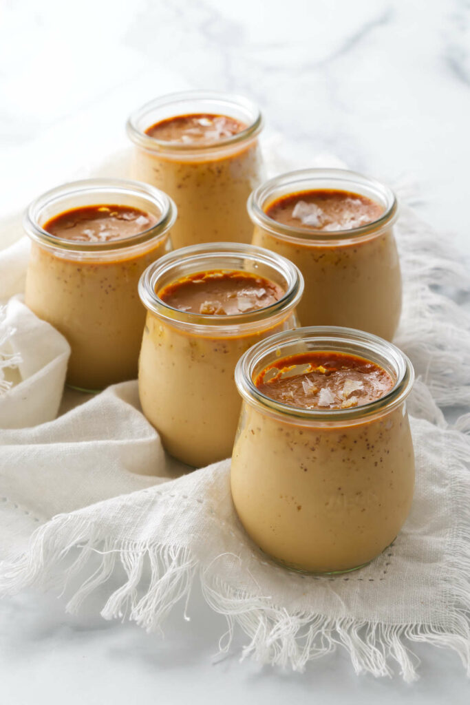 Several jars of baked caramel custard topped with flaky salt.