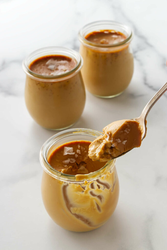 A spoon scooping some custard pudding caramel in a jar.