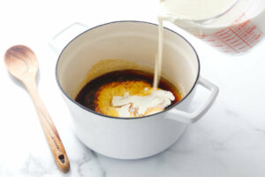 Adding cream to homemade caramel in a large pot.