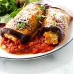 Two sausage stuffed eggplant rolls on a dinner plate.