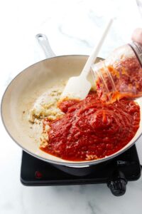 Adding marinara sauce to a skillet.
