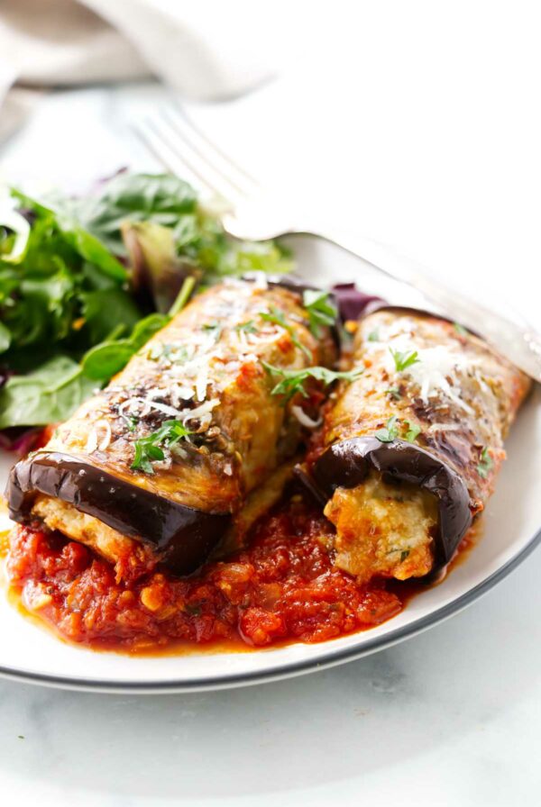 Two sausage stuffed eggplant rolls on a dinner plate.