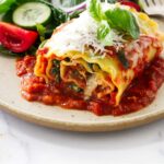 A stuffed lasagna roll on a dinner plate with a salad.