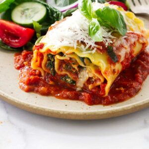 A stuffed lasagna roll on a dinner plate with a salad.