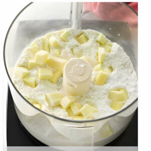 Adding cubed butter to the flour mixture in a food processor.