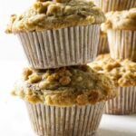 Two crumb-topped muffins stacked, more muffins blurred in the background.