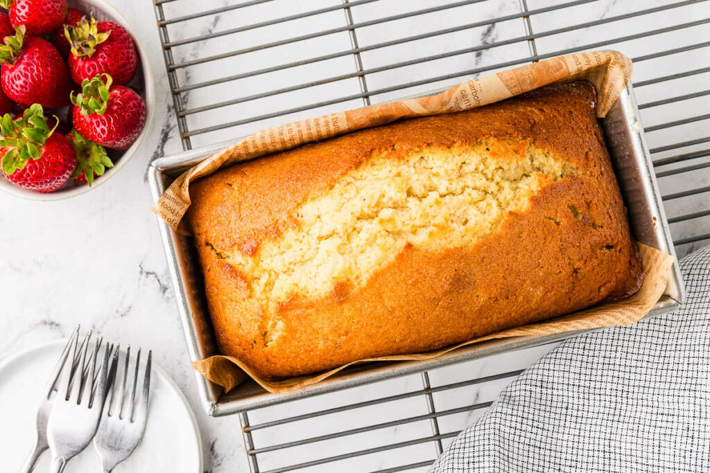 A sourdough pound cake on a cooling rack next to strawberries.
