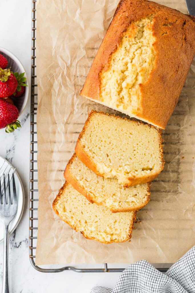 Partially sliced sourdough pound cake on a cooling rack with parchment paper.