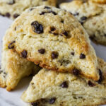 Close-up of stacked chocolate chip scones with crumbly texture on white surface.