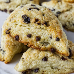 Close-up of stacked chocolate chip scones with crumbly texture on white surface.