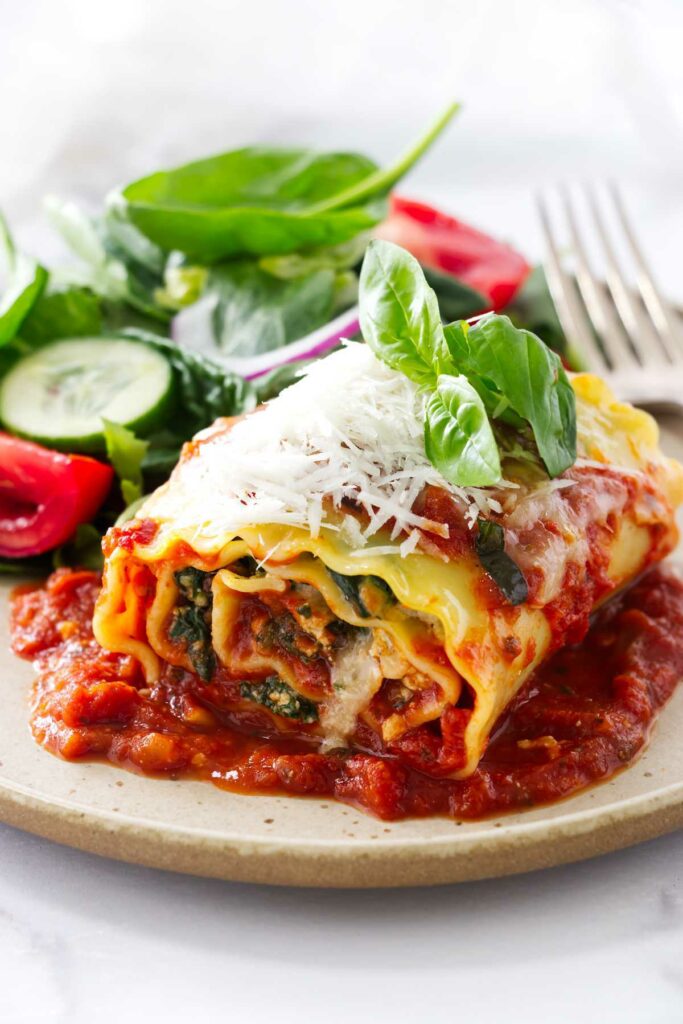 A stuffed lasagna roll-up on a plate with a salad.