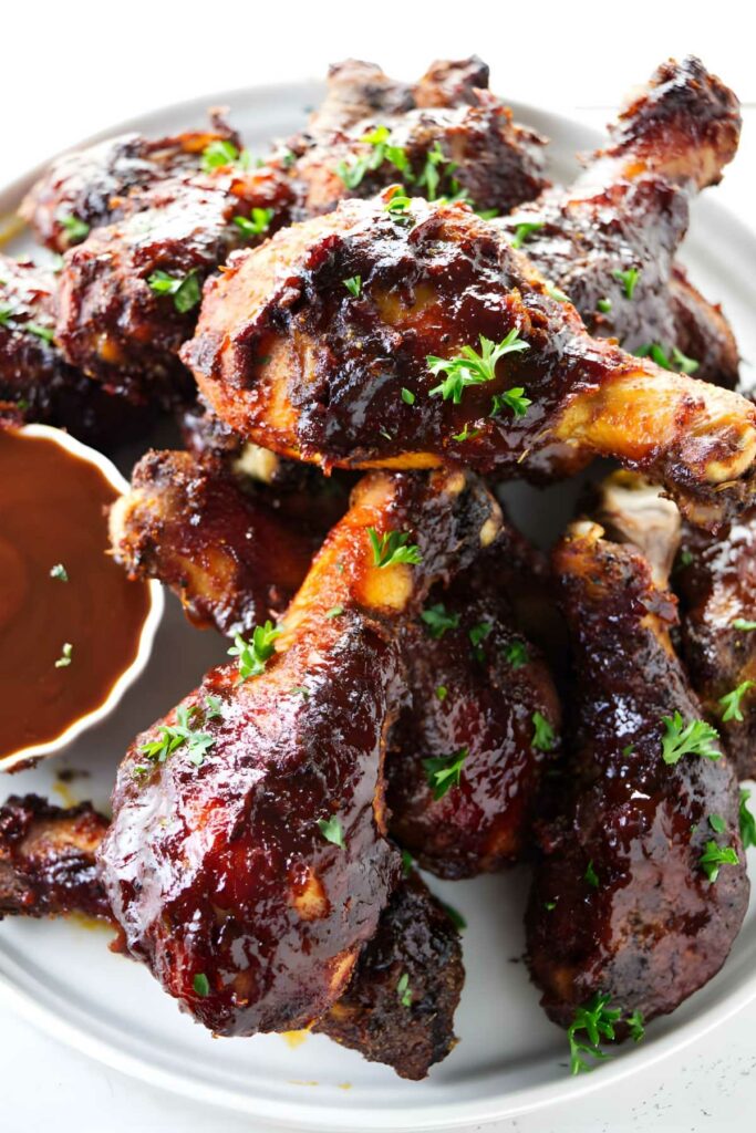 Glazed barbecue chicken drumsticks on a plate with parsley and sauce.