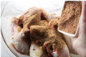 Raw chicken pieces in a bowl sprinkled with dry spices.