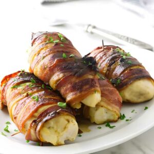 Bacon-wrapped, cheese-stuffed chicken breasts on a white plate with parsley.