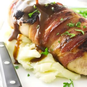Bacon-wrapped chicken on mashed potatoes with gravy and parsley garnish.