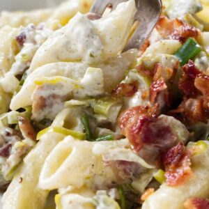 Creamy penne pasta with bacon, leeks, and white sauce on a fork.