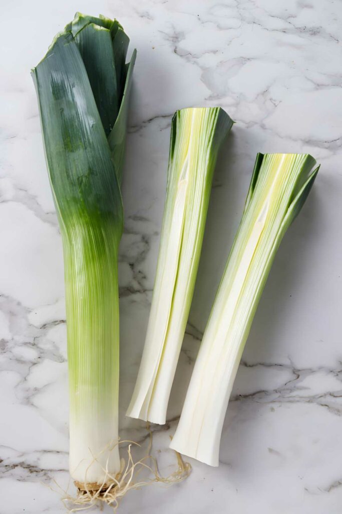A leek being sliced in half next to a whole leek. 