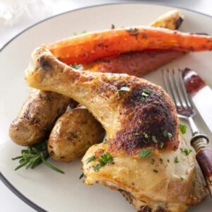 Roasted chicken leg, potatoes, and carrots on a plate with utensils.