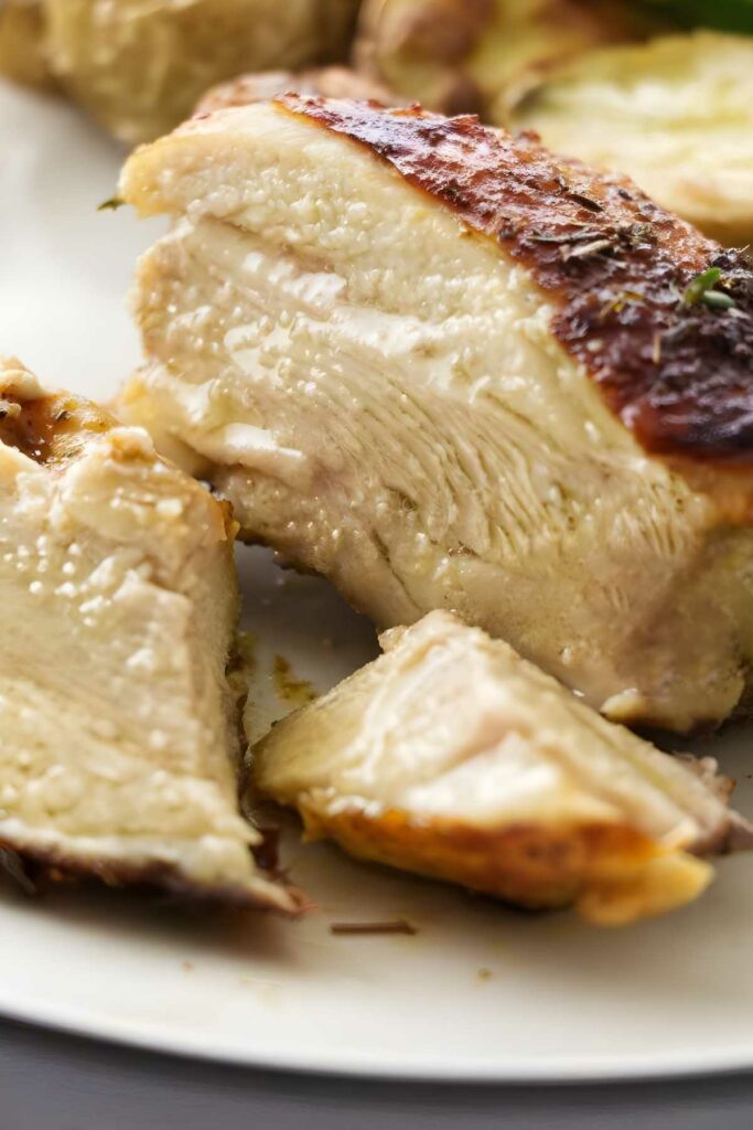 Sliced roasted chicken thigh with crispy golden skin on a white plate.
