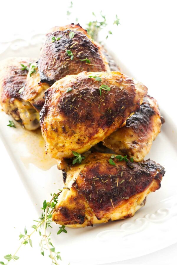 Roasted chicken thighs with crispy skin on a white platter, garnished with thyme.
