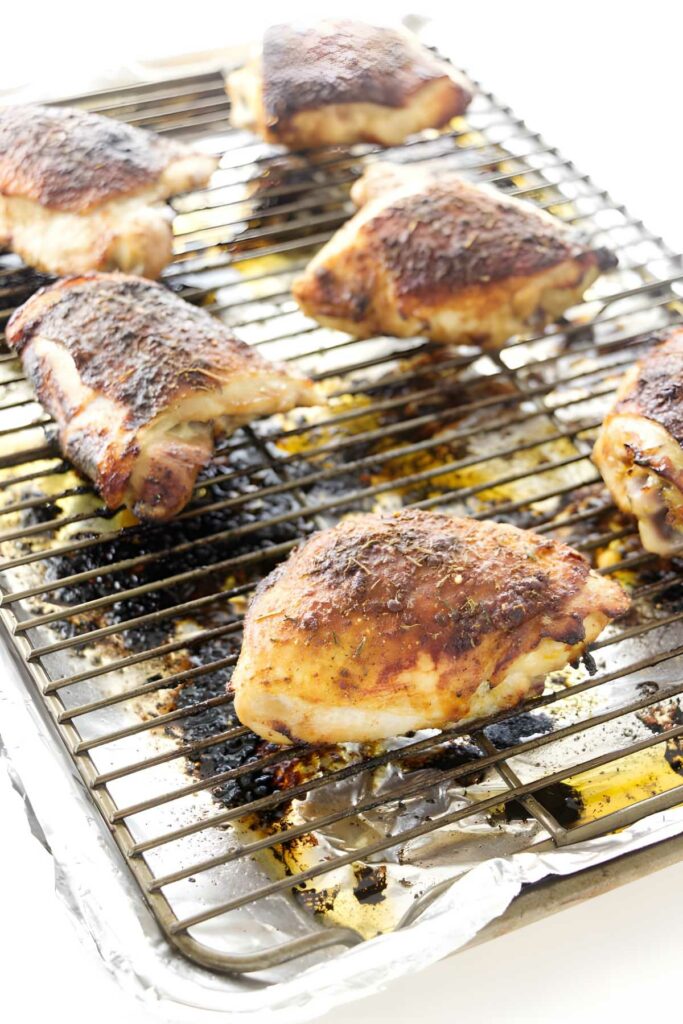 Browned chicken thighs resting on a wire rack above a foil-lined pan.