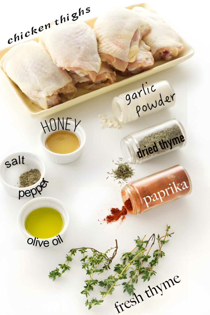 Raw chicken thighs on a plate with labeled spices and seasonings around them.