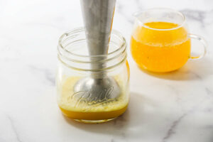 An immersion blender in a jar in front of melted hot butter.