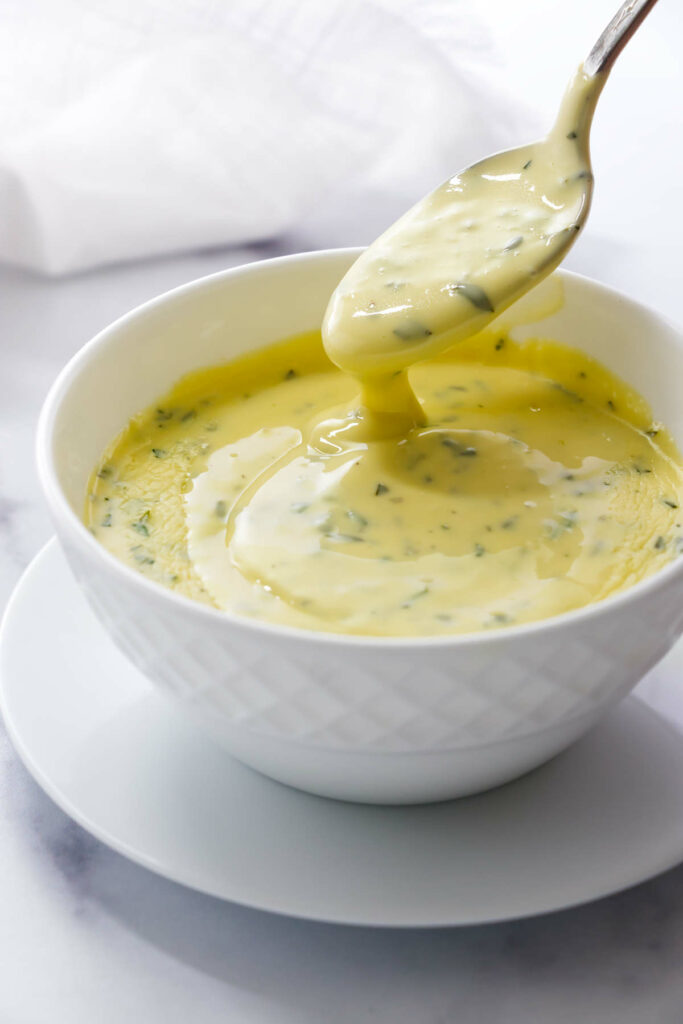 A spoon drizzling easy Béarnaise sauce into a bowl.