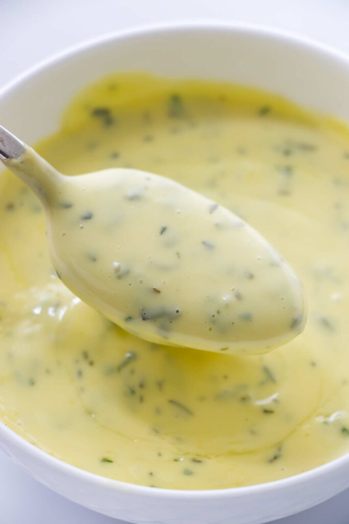 A spoon in a bowl of immersion blender Béarnaise with tarragon.
