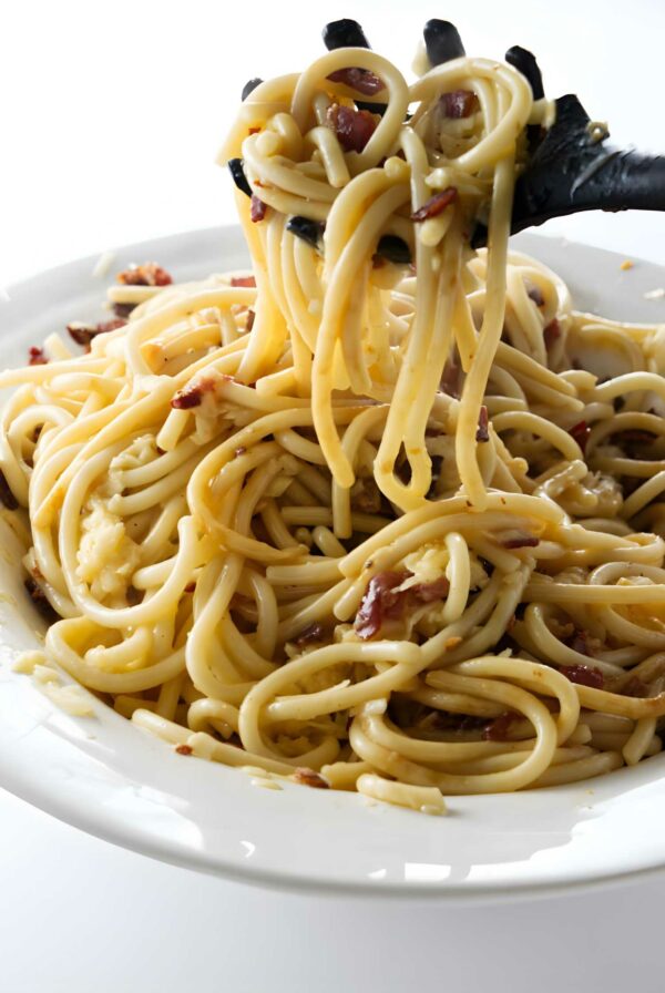 Close-up of creamy bucatini carbonara with bacon lifted by black utensil.