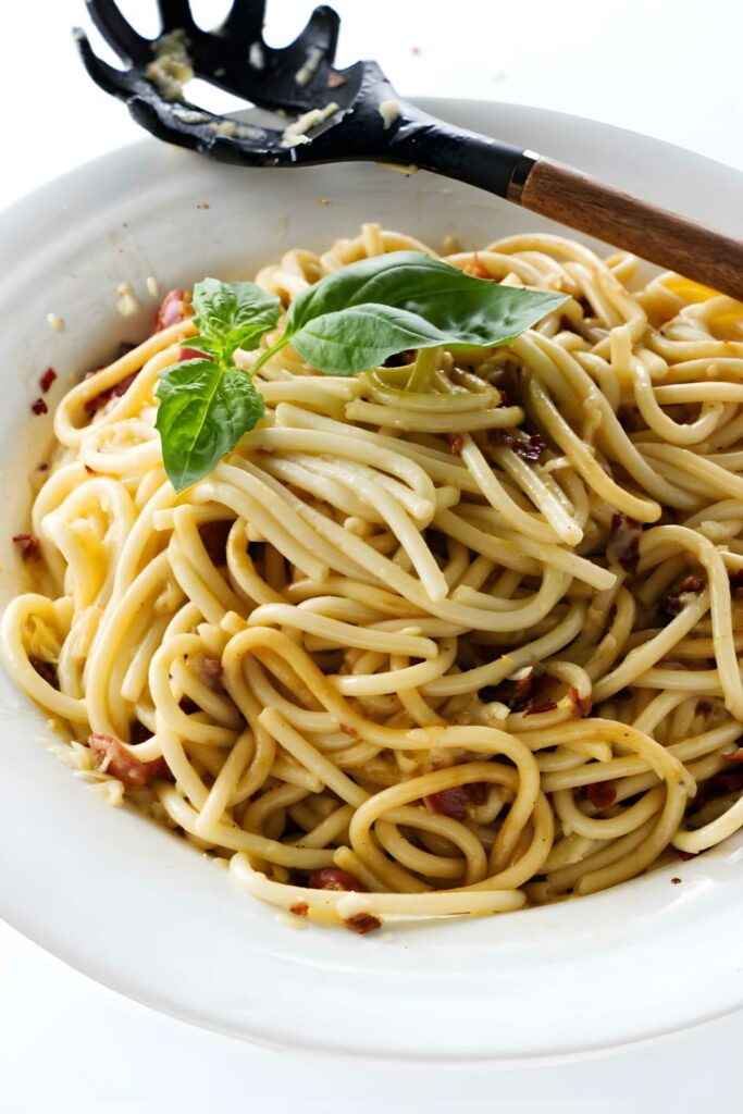 Bucatini in a white bowl with basil garnish and serving spoon.