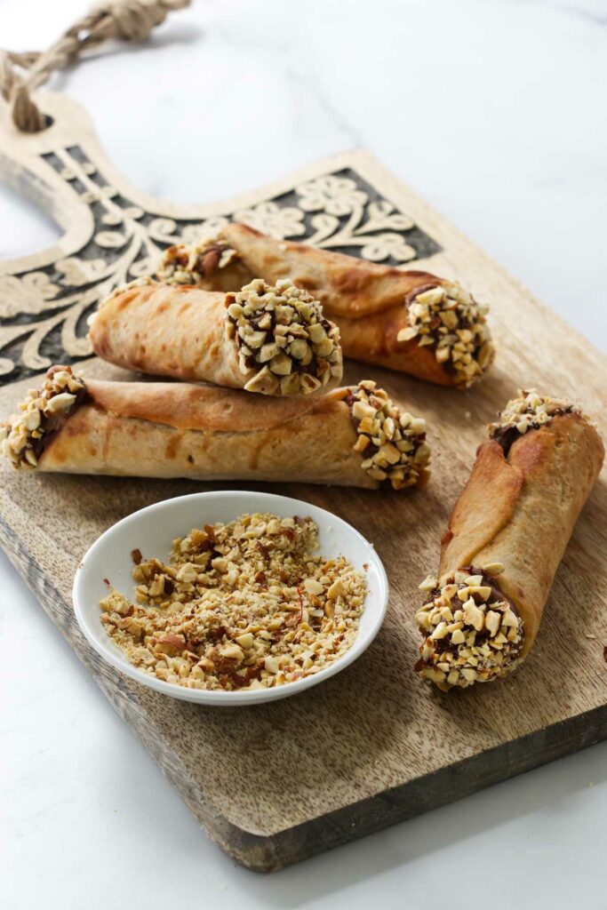 Dipping chocolate filled cannoli in crushed hazelnuts.