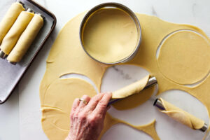 Rolling cannoli dough around pastry tubes.