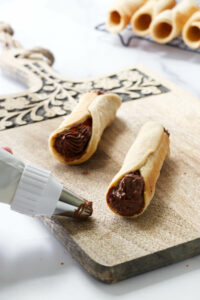 Filling canolli shells with chocolate hazelnut cream.