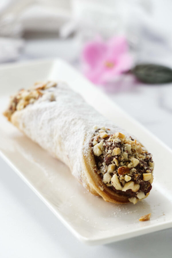 A chocolate hazelnut cannoli on a plate dusted with powdered sugar.