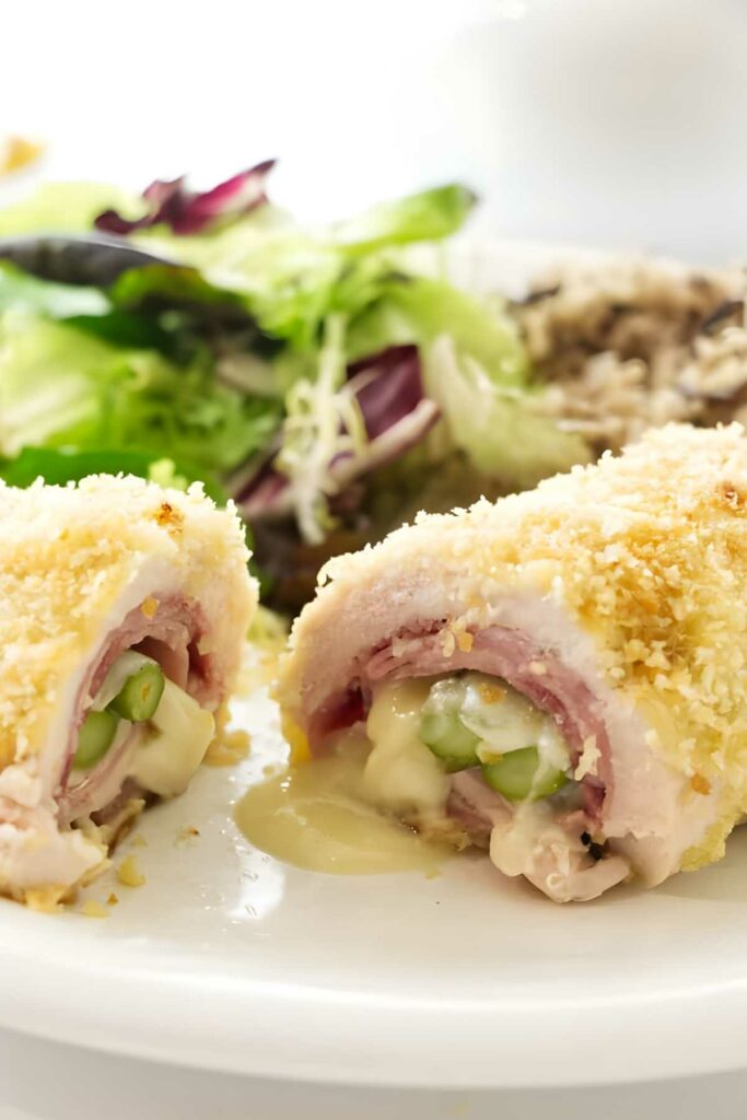 Sliced chicken cordon bleu asparagus, ham, and asparagus on a white plate.