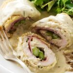 Chicken roulade with ham, asparagus, and sauce, served with mixed greens.
