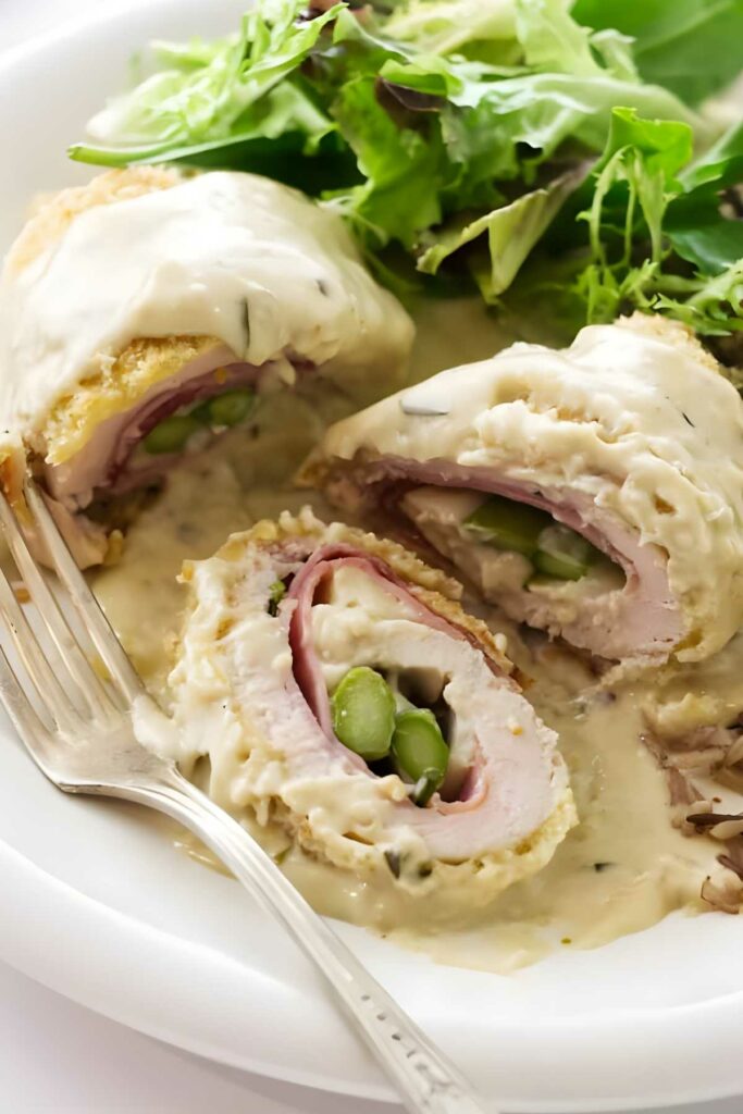 Chicken roulade with ham, asparagus, and sauce, served with mixed greens.