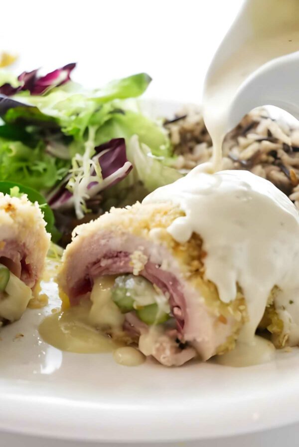 Close-up of asparagus chicken cordon bleu with creamy sauce, mixed greens, and wild rice.