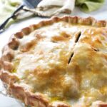 Golden-brown baked pie in a clear dish on white surface.