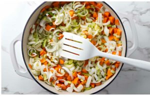 White pot of chopped vegetables stirred with spatula.