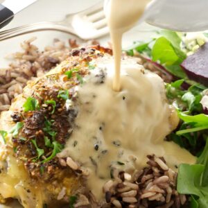 White wine sauce poured on chicken thigh with wild rice and salad.
